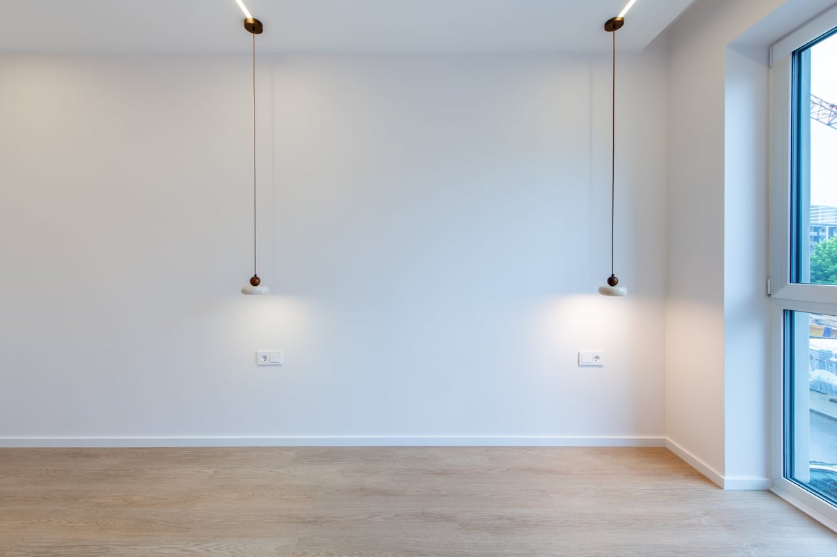 A spacious, empty room featuring a wooden floor and minimalist pendant lights suspended from the ceiling, captured with soft lighting for a sleek, clean, and modern aesthetic.